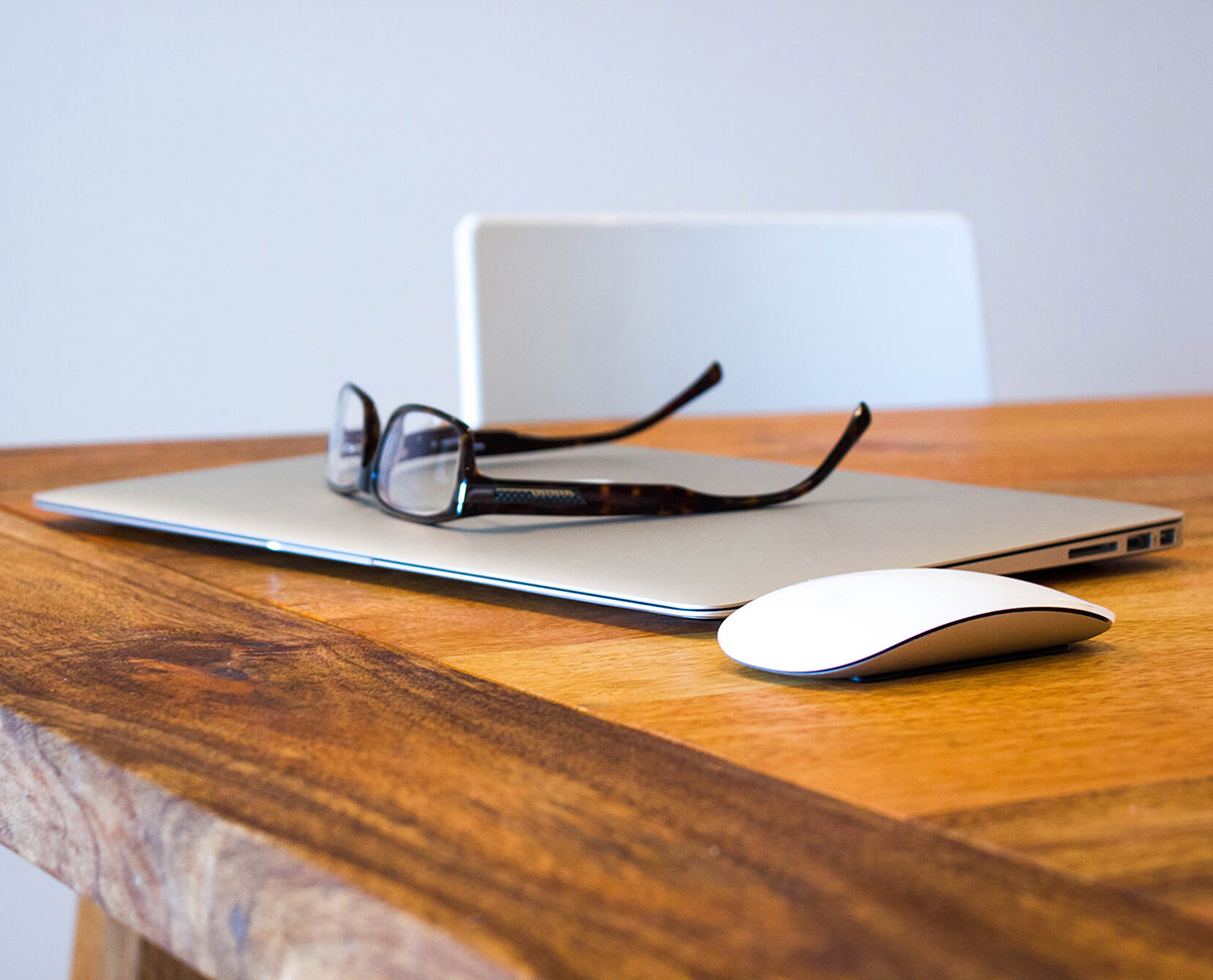 professional setting, desk with apple laptop with eye glasses on top